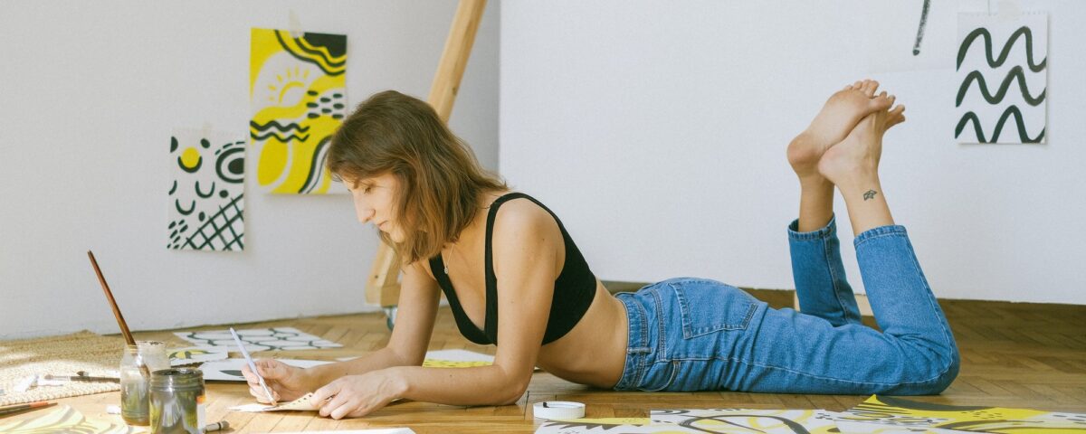 woman lying on the floor while doing artwork